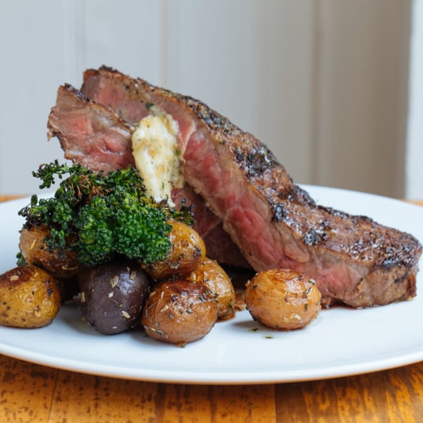 Mercato's sliced steak with roasted potatoes, broccolini, and a dollop of butter on a white plate.