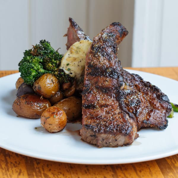 Grilled steak with roasted potatoes, broccoli, and a dollop of sauce on a white plate.