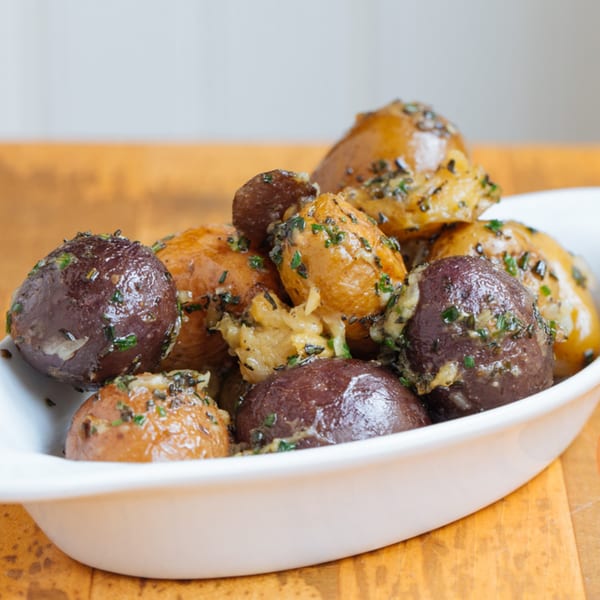 A white bowl filled with roasted brown and purple potatoes, garnished with herbs and garlic.