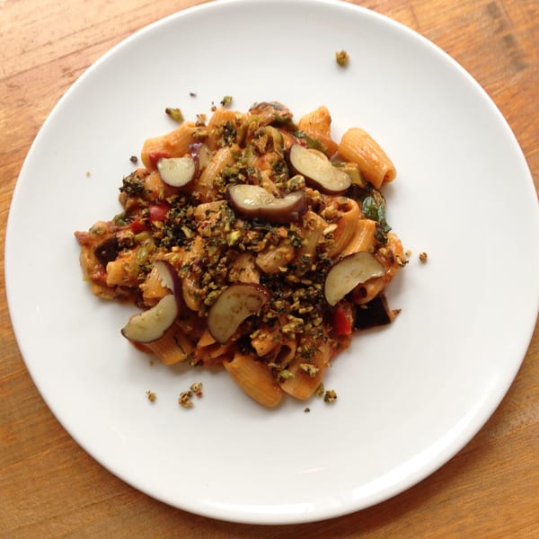 Mercato's rigatoni pasta with eggplant, red sauce, and green herbs on a white plate.