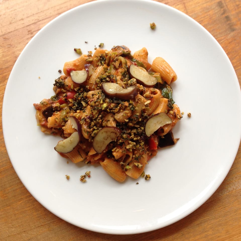 Mercato's rigatoni pasta with eggplant, red sauce, and green herbs on a white plate.
